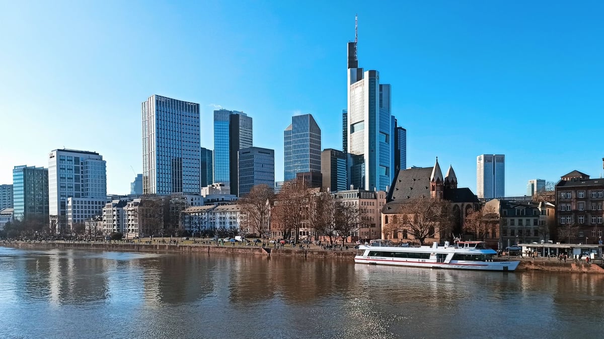 Frankfurter Skyline mit modernen Wolkenkratzern, gespiegelt im Main, mit weißem Ausflugsboot im Vordergrund